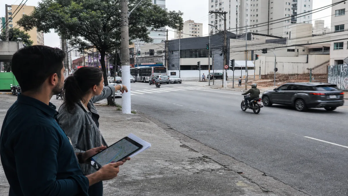 Analistas discutem simulação de fluxo urbano em avenida de São Paulo, observando tráfego e utilizando tablet